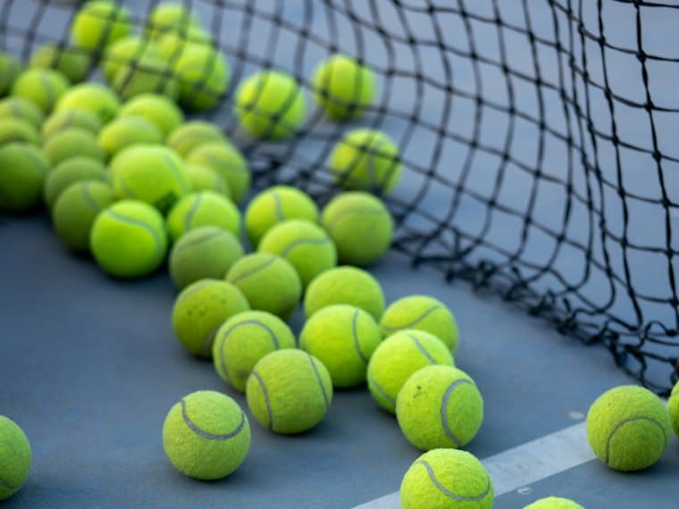 Pelotas de tenis repartidas sobre una cancha azul junto a la red.
